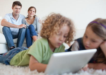 Cute children using a tablet computer while their happy parents are watching
